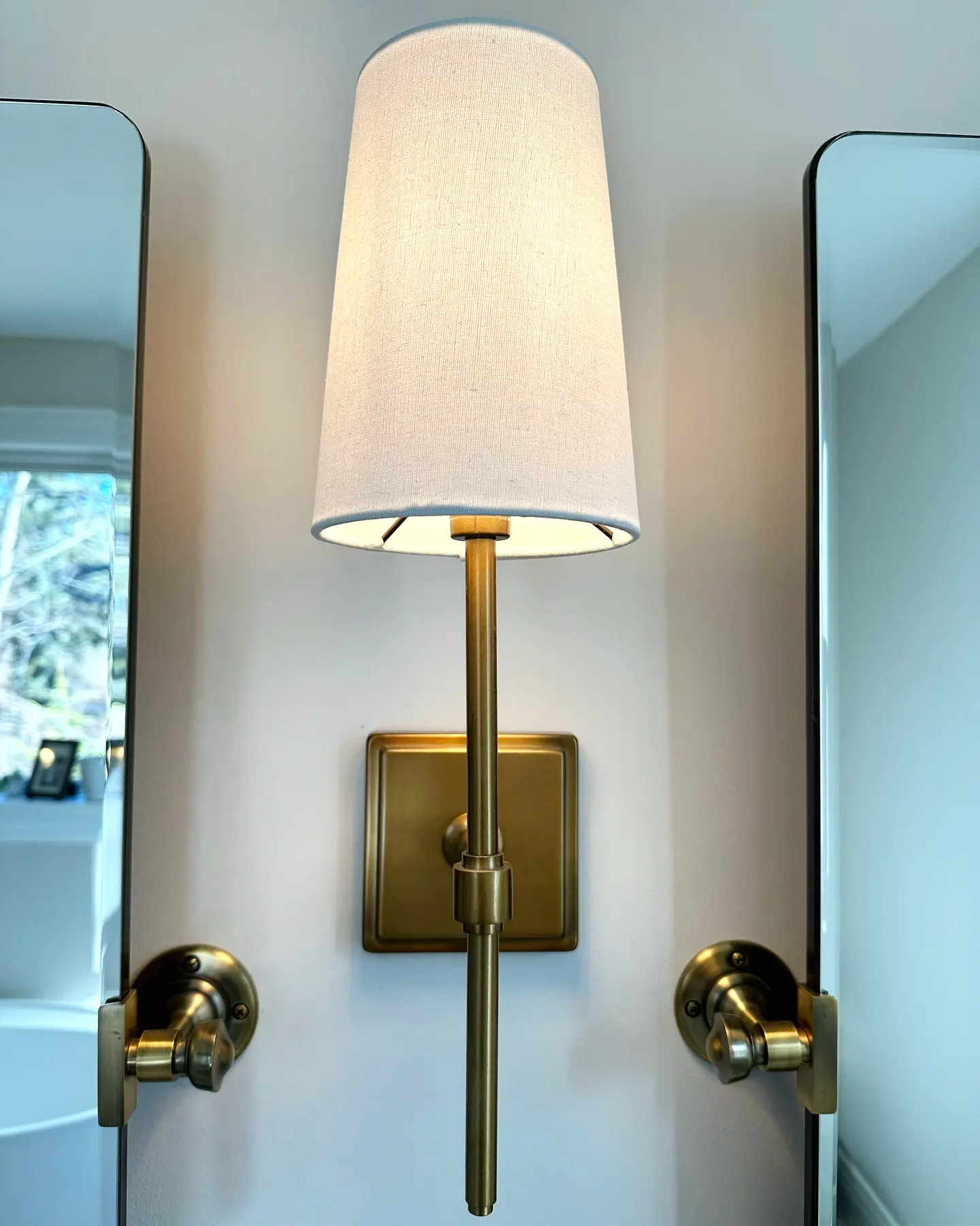 Brass wall sconce installed between two mirrors